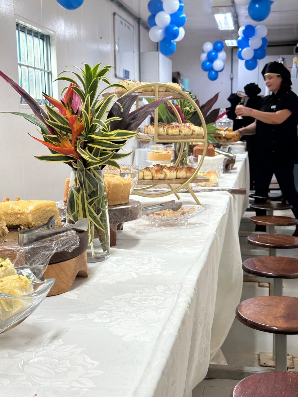 Mesa de café da manhã montada pela Valverde em evento, com pães, bolos e arranjo de flores